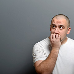 Portrait of a man biting nails and being scared against gray bac