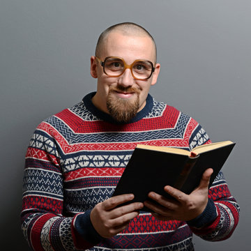 Portrait of a nerd holding book with retro glasses against gray
