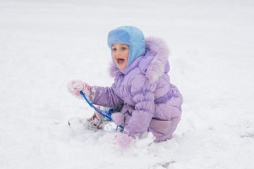 Fototapeta na wymiar Happy little girl slid down the icy hill and happily watching the other children