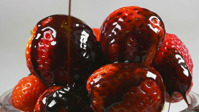 Delicious melted chocolate syrup pouring over strawberries in reverse