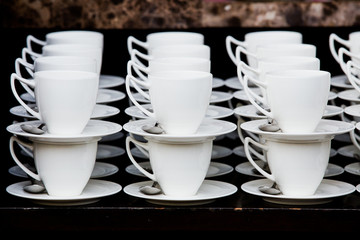 Many white coffee cups in a line over a buffet