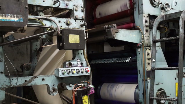 Locked down shot showing the turning cyan and magenta drums of an industrial offset press newspaper printing machine.
