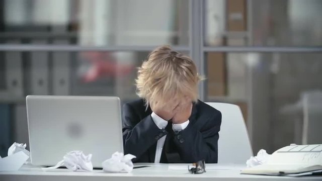 Little office worker found a mistake in his business project and covering face with hands in front of the laptop