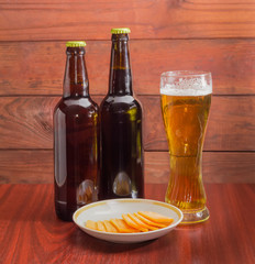 Glass and two bottles of beer, cheese on wooden surface