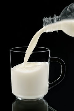Молоко наливается из бутылки в бокал, на чёрном фоне