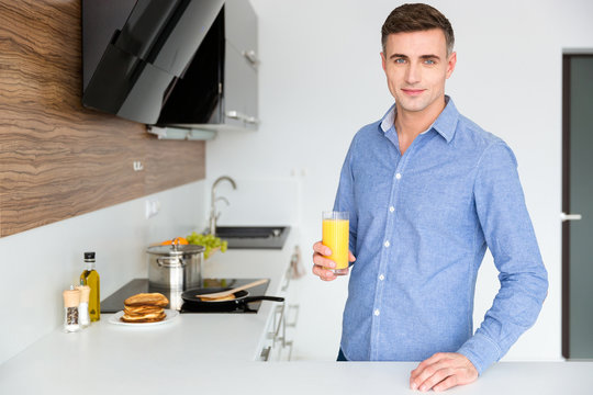 Handsome man standing on the kitchen and drinking juice