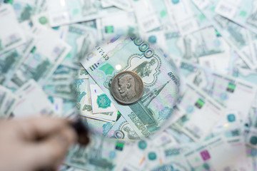 Foreign coin in a magnifying glass against the background of Russian rubles.