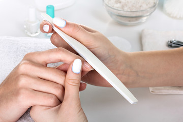 Closeup shot of a woman in a nail salon receiving a manicure by a beautician with nail file. Woman...