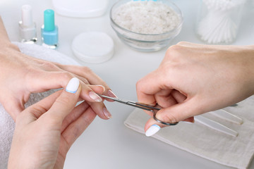 Closeup shot of a woman in a nail salon receiving a manicure by a beautician with nail scissors. Woman getting nail manicure. Beautician file nails to a customer.