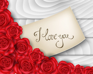 Love note on paper between red roses on white wood background