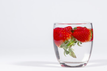 Water glass with several floating strawberries, blank space at left