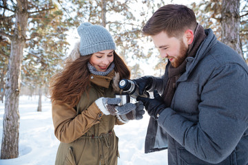 Happy couple drinking hot tea in winter park