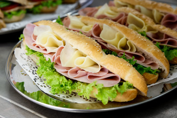 Yellow sliced cheese, ham and salad white  baguettes on doily and stainless steel tray.