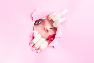 Young woman looking thru torn pink cardboard