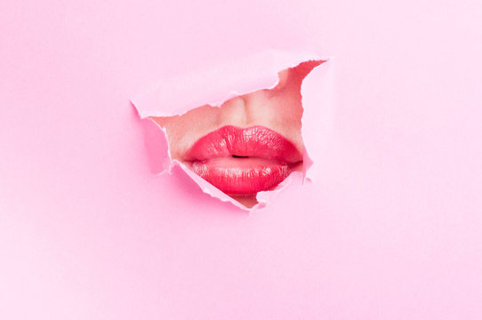 Attractive female mouth sharing a kiss thru ripped paper hole