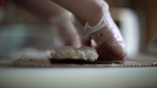 A sushi chef prepares rolls with a bamboo mat, he lays out the rice on a sheet of Nori seaweed and puts on the rice red fish
