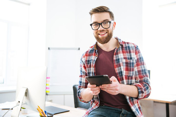 Cheerful male sitting and holding tablet in the office