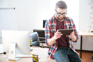 Smiling bearded man sitting with tablet on table in office