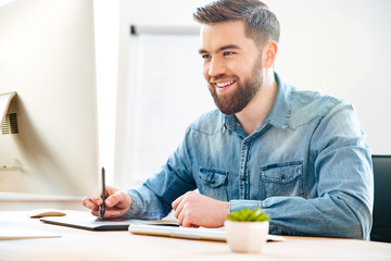 Happy male designer sitting and drawing on graphic tablet