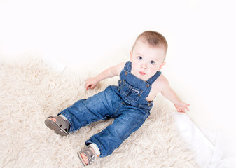 Naklejka premium Cute baby with big blue eyes in denim overalls sitting isolated on white background.