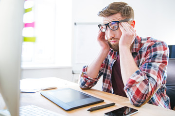 Tired exhausted man sitting on workplace and touching temples