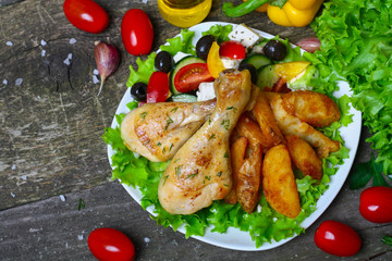 roasted chicken legs with potatoes with Greek salad on wooden background with vegetables