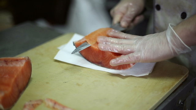 The chef cuts knife a fillet of red fish into pieces for making sushi and rolls
