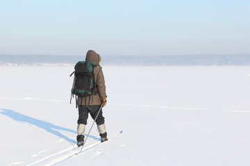 Fototapeta na wymiar The man the traveler with a backpack skiing on snow of the frozen river 