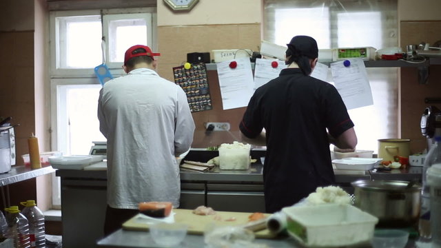 Two sushi chefs cook sushi and rolls in the kitchen
