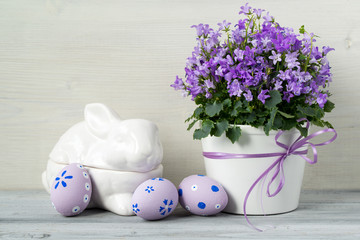 Beautiful easter decoration with Campanula flowers, Easter eggs and ceramic rabbit, on white wooden background