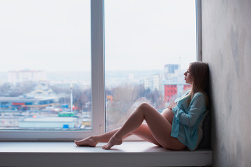 Pregnant girl sitting on the window sill