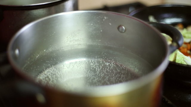 Water is heated in a saucepan on the gas stove, air bubbles rise to the water surface

