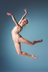 Young beautiful modern style dancer jumping on a studio background