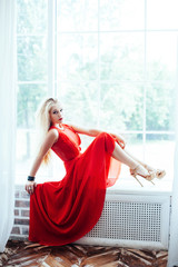 young sexy blonde woman with red lips in red dress posing in int