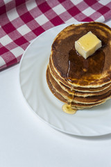 Stack of homemade pancakes with butter and honey on white plate with checkered napkin. Russian holiday pancake week. Vertical view.