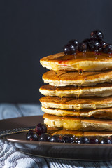 Stack of homemade pancakes with berries and honey on brown plate on rustic background. Russian holiday pancake week. Focus on pancakes. Vertical view.