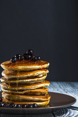 Stack of homemade pancakes with berries and honey on brown plate on rustic background. Russian holiday pancake week. Focus on pancakes. Vertical view.