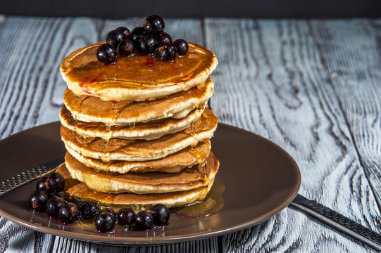 Stack of homemade pancakes with berries and honey on brown plate on rustic background. Russian holiday pancake week. Focus on pancakes. Horizontal view.