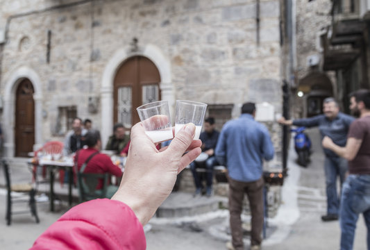 CHIOS ISLAND, GREECE - APRIL; Greek men having fun in a bbq party in street of the Pirgi town in Chios Island, Greece. A hand holding Mastic liquor that is traditional drink in Chios Island.