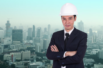 engineer in helmet with arms crossed, city background