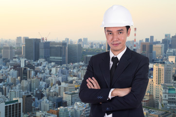 engineer in helmet with arms crossed, city background