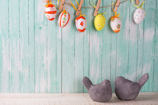 Two decorative birds and colorful easter eggs on rope on wooden
