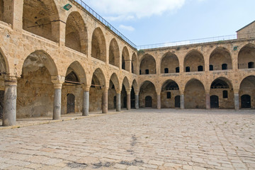 Fototapeta na wymiar Arched gallery of Khan al-Umdan viewed from paved courtyard. Old city of Acre, Israel. 
