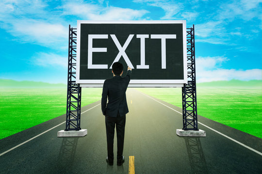 businessman standing on road and pointing with large sign of exi