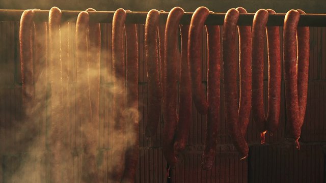 Smoking homemade pork sausages, food preparation process of cured pork meat delicacy in smokehouse.