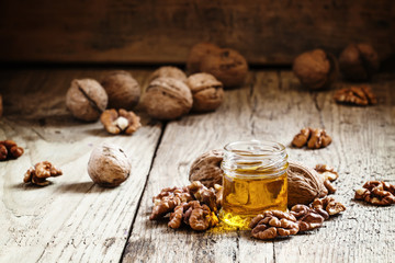 Walnut oil in a small jar and kernels on old wooden background i