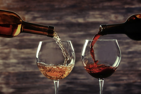 White and red wine pouring in glasses on wooden background