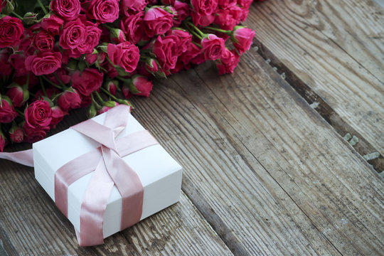Holiday background with pink roses and gift box over wooden tabl