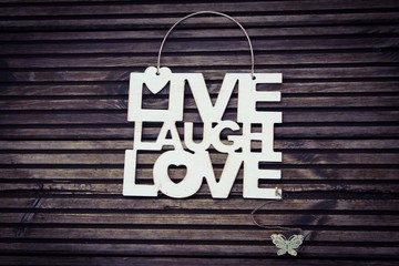 Metal sign with the words LIVE LAUGH LOVE with a metal butterfly on a wooden surface