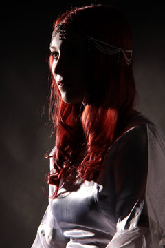 Eine Frau im Profil mit roten Haaren im weißen Kleid halbschattig sitzend